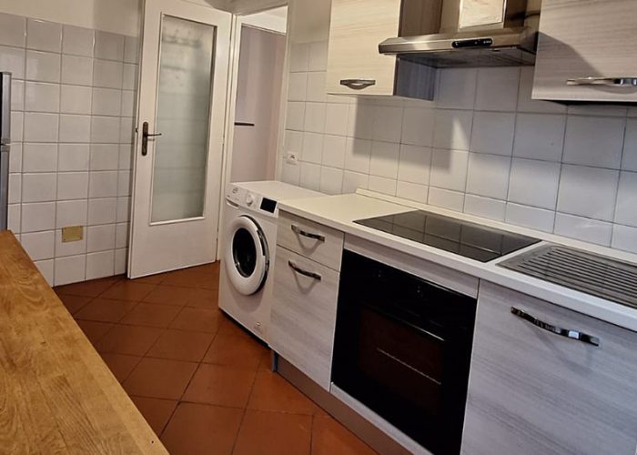 cucina moderna con lavatrice, forno, piano cottura a induzione e mobili chiari di una delle nostre Case Vacanza a Ladispoli