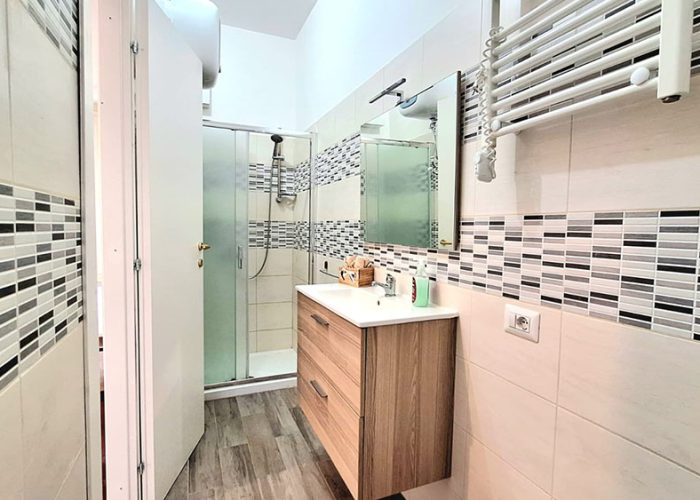 secondo bagno dell’appartamento Terrazza del Mare con doccia, mobile lavabo in legno e rivestimento moderno, in una delle nostre case vacanza a Ladispoli